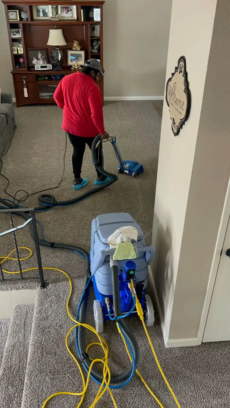 Technician in red shirt using a carpet cleaning wand and extractor on beige residential carpet in a living room