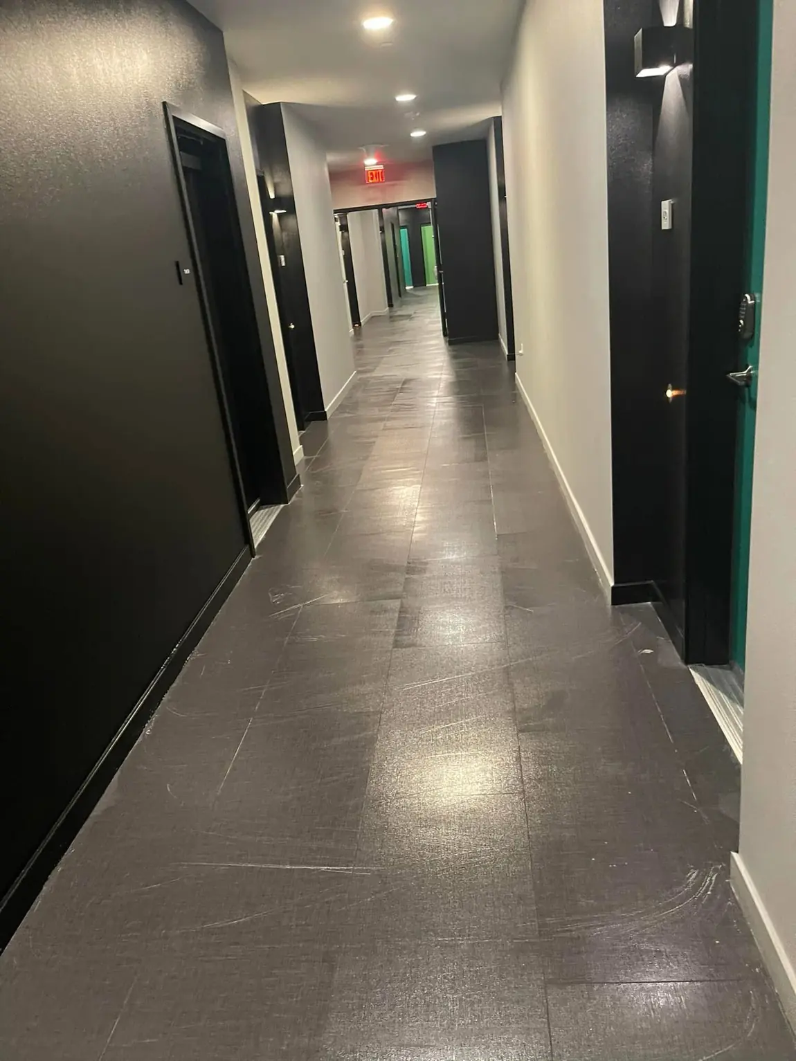 Clean commercial hallway with dark tile floor, recessed lighting, and multiple office doors for janitorial cleaning