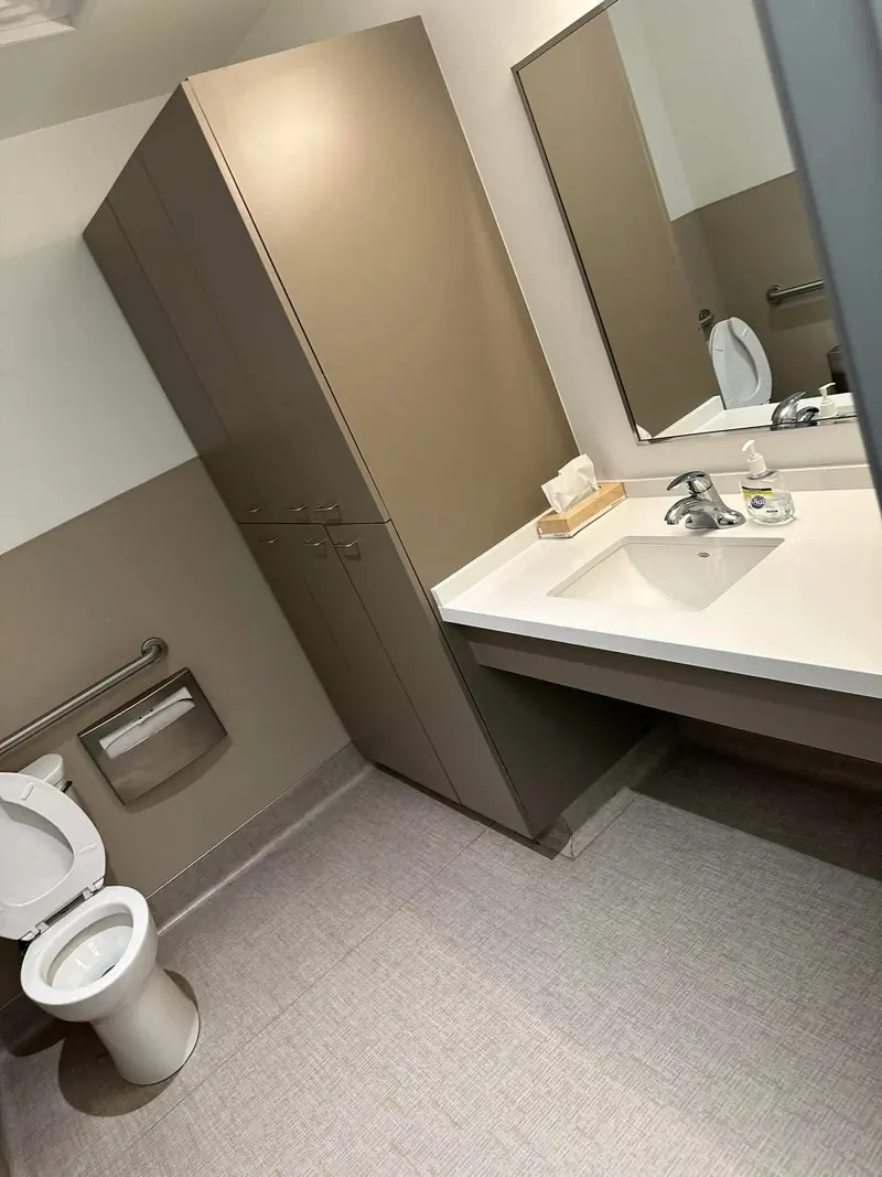 Clean medical office restroom with white sink, soap dispenser, tissue box, toilet and beige cabinetry for janitorial cleaning