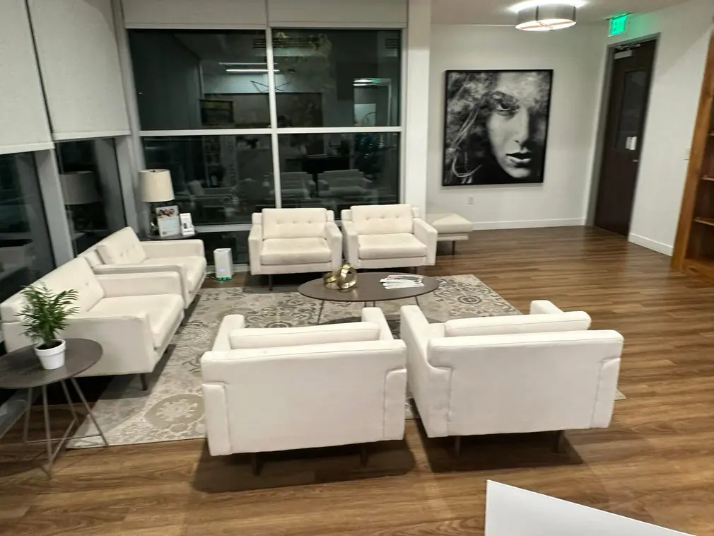 Modern office reception area with cream armchairs, coffee table, large window and framed wall art, spotless hardwood floor