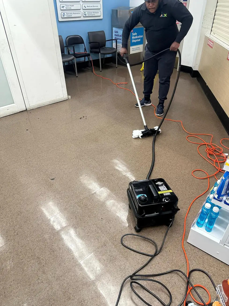 Technician using a floor scrubber and wand to deep-clean a retail facility floor near seating and product displays