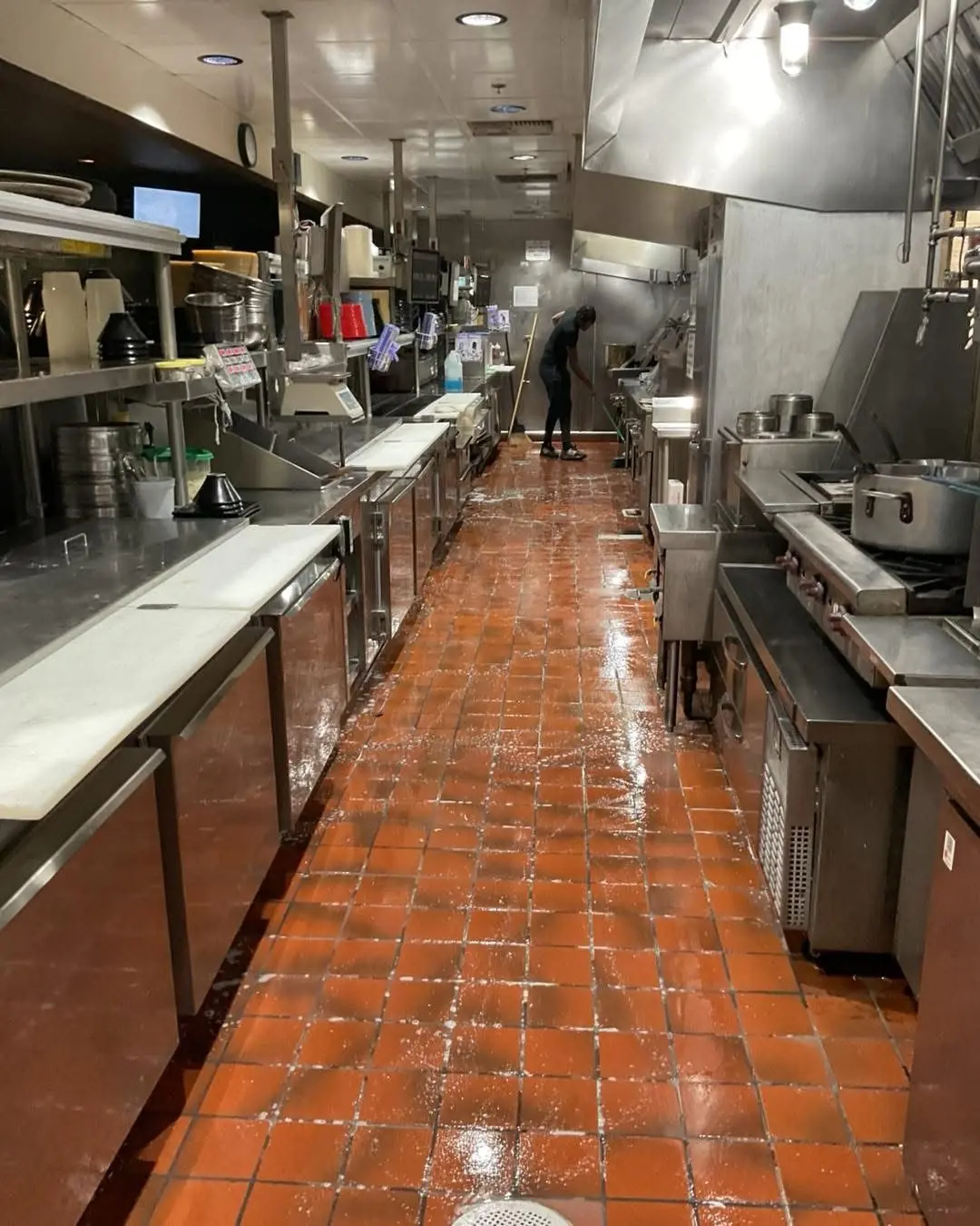 A commercial kitchen with wet tiled floor being mopped by a cleaner during janitorial cleaning service