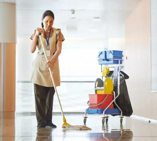 A janitorial worker mopping a bright commercial hallway next to a cleaning cart for office cleaning services
