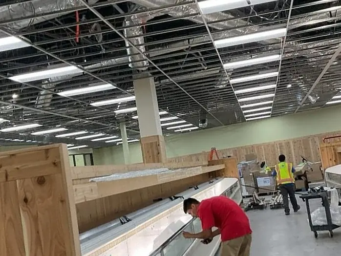 Worker in red shirt wiping a long display case in a large post-construction commercial retail space with exposed ceiling