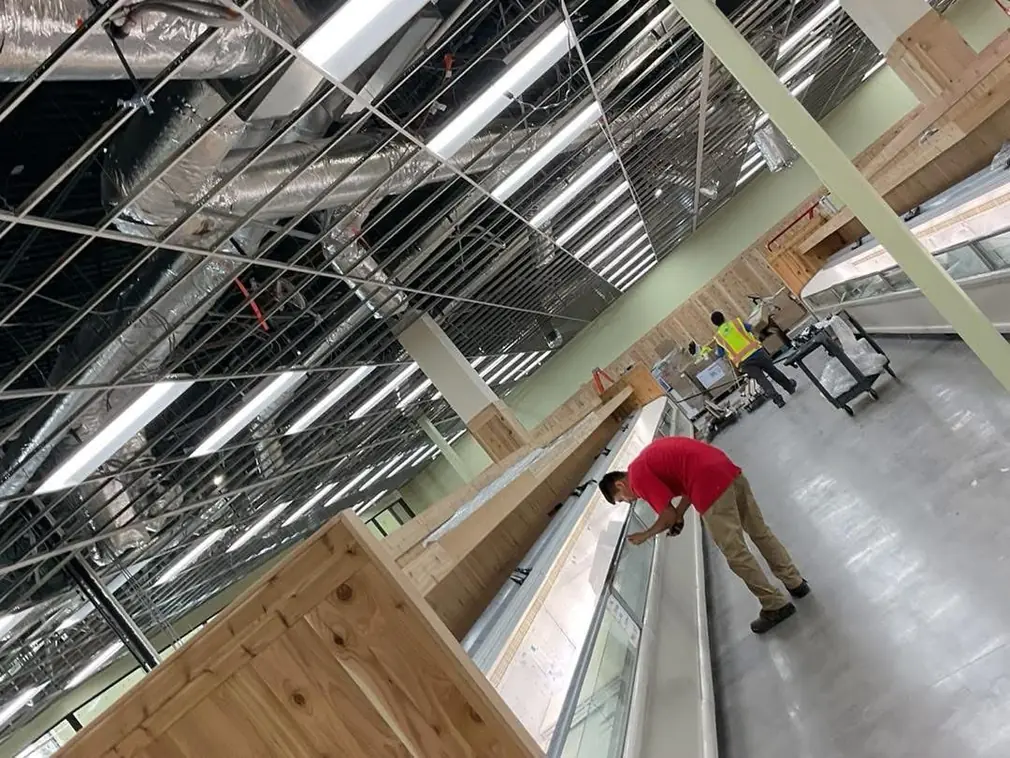 Worker in red shirt cleaning display cases during post-construction commercial cleaning in a large retail space