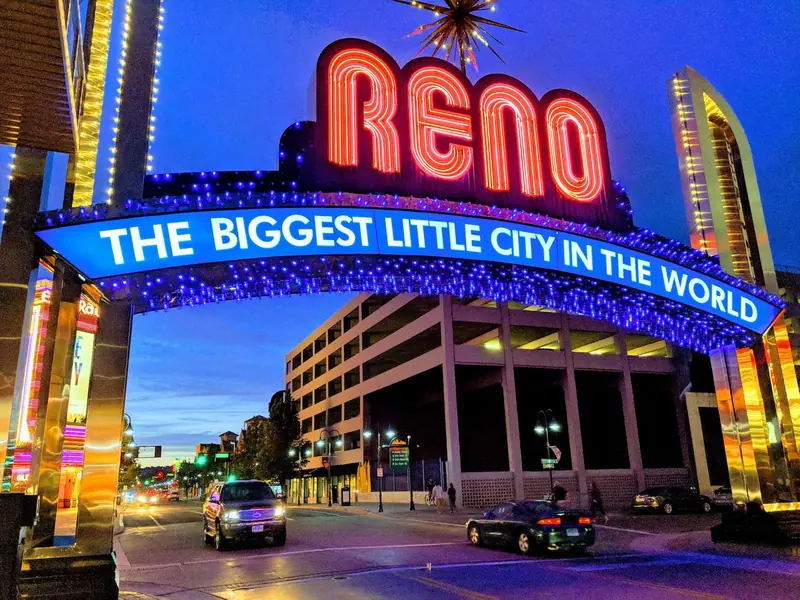 Reno neon arch at dusk reading "The Biggest Little City in the World" over a downtown street scene, cars passing