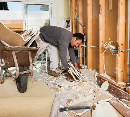 Cleaning crew member removing drywall rubble and sweeping an office renovation site for post-construction cleaning